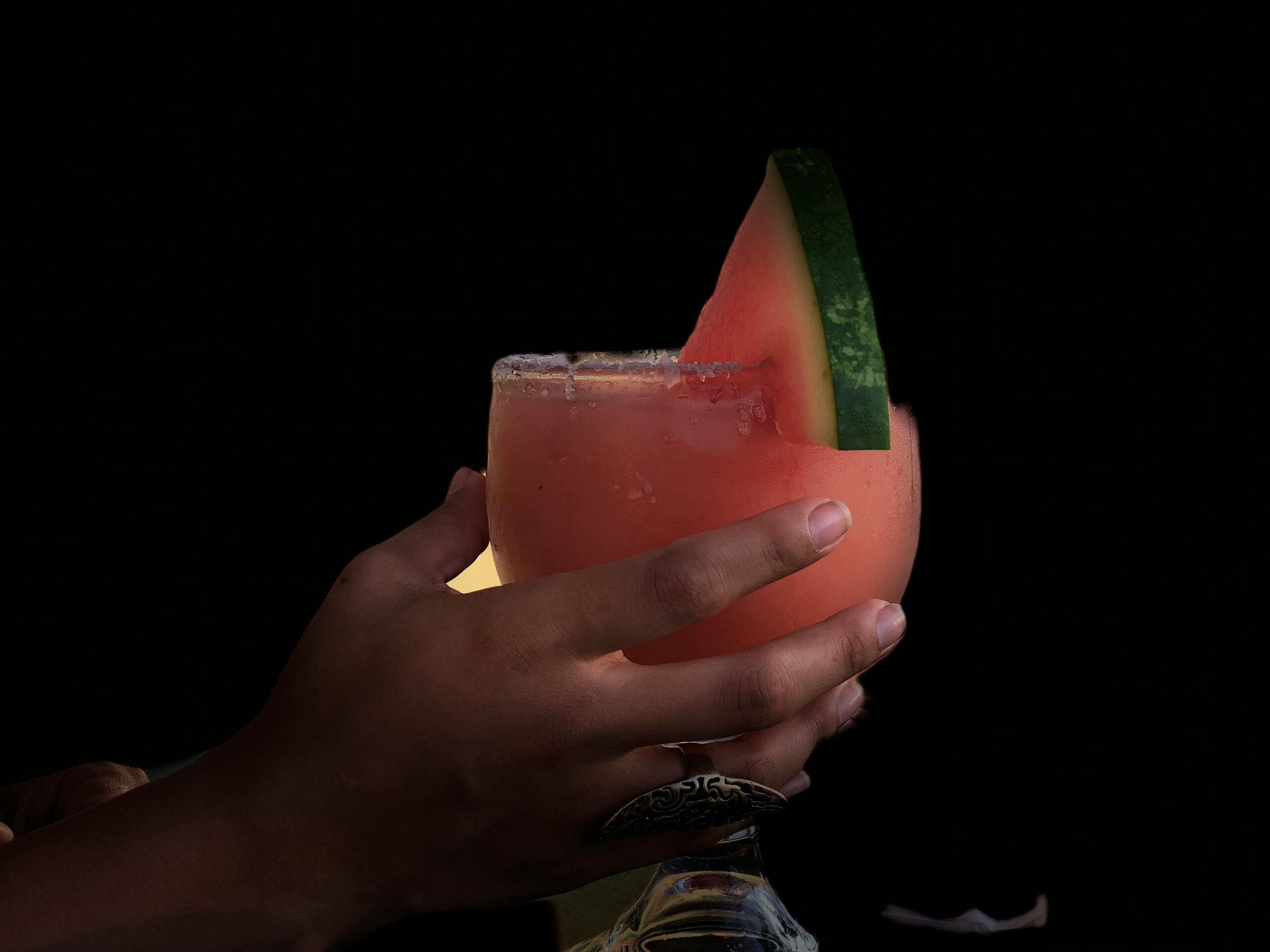 Hand holding a refreshing watermelon cocktail garnished with a slice.